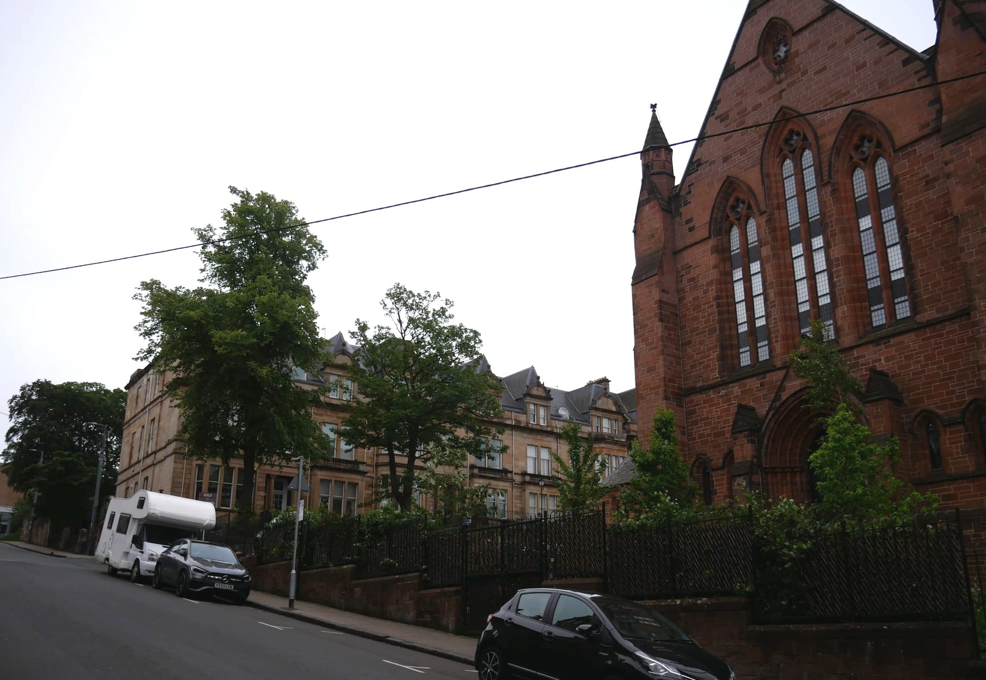 On the right is a red sandstone church from the 1800s. To the left and slightly uphill is a blond sandstone of a Glaswegian Georgian Terrace.
