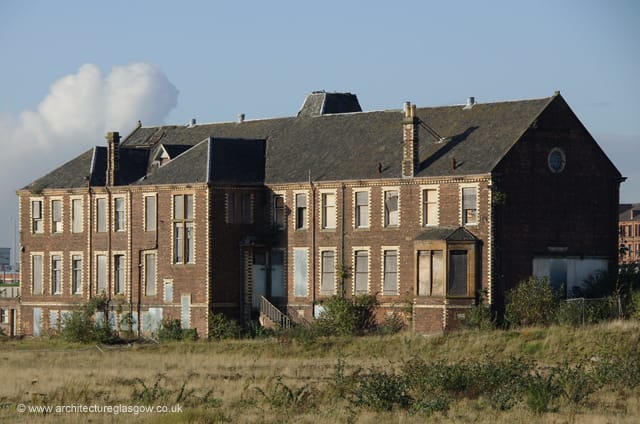 An old brick shipyard office building sits on a brownfield site in Glasgow. The windows are boarded up but it looks otherwise in fair condition. 