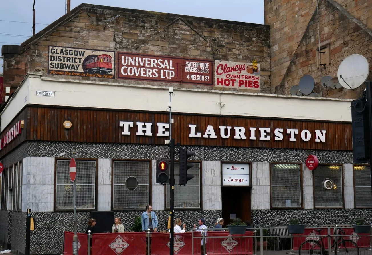 A picture showing the front facade of classic Glasgow pub The Laurieston. People are drinking outside. 
