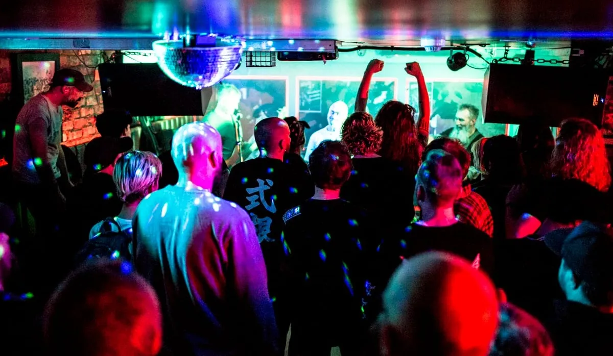 A small venue hosts a band with a small but attentive crowd. There's a disco ball and the ceiling is very low. 